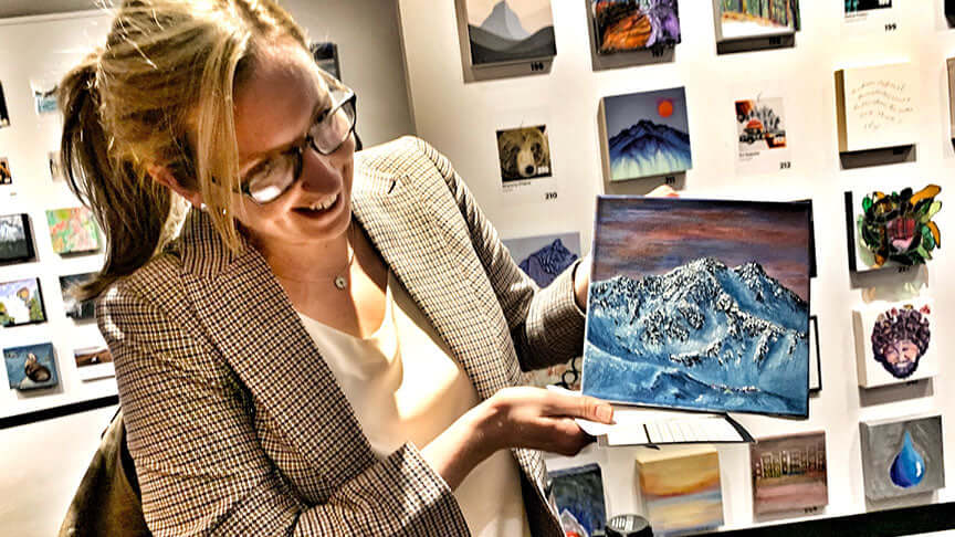 Woman holding a commission painting of a mountain by graham watts in an art gallery.