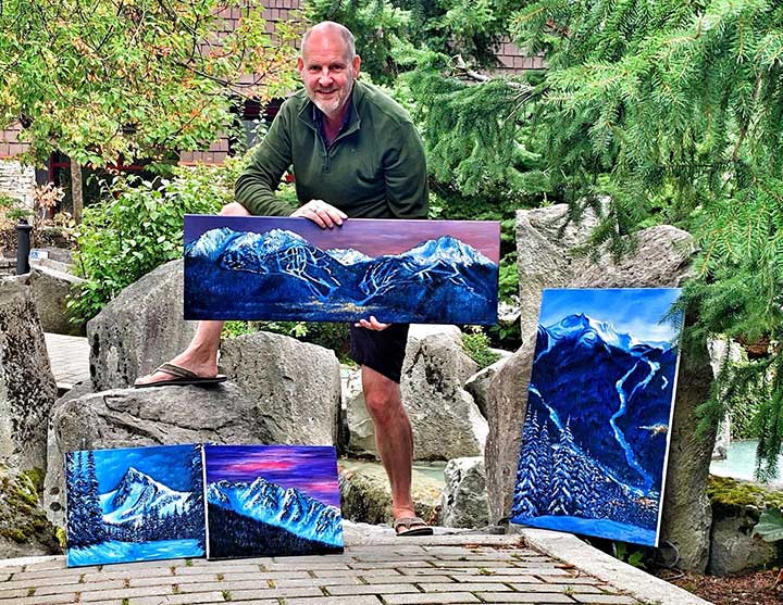 canadian artist graham watts  holding a painting of mountains in a garden setting whistler bc